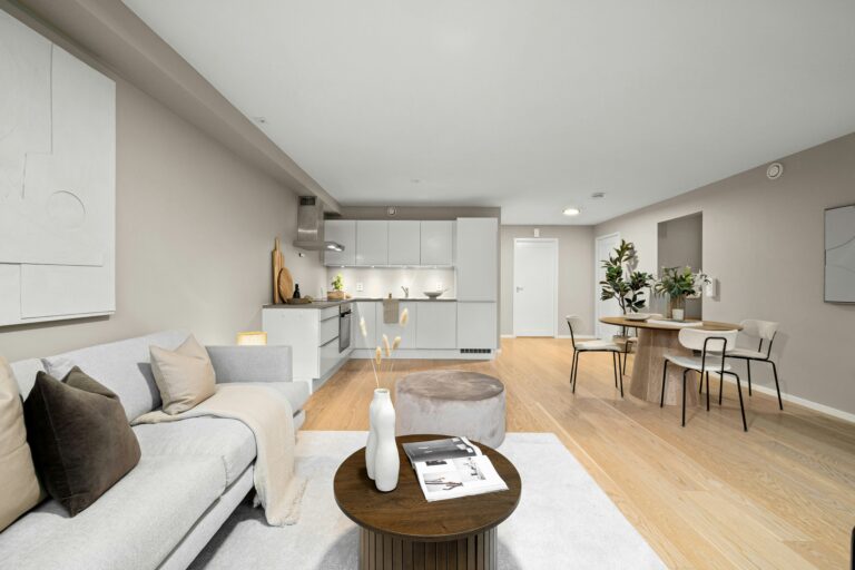 Open concept remodel featuring a neutral living area with a grey sofa and round coffee table, opening up to a minimal white kitchen and a separate dining area with a round wooden table.