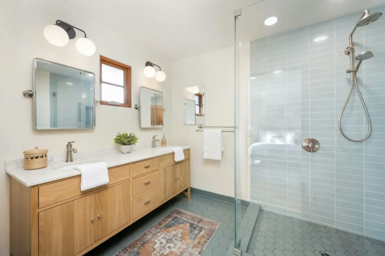 Modern bathroom featuring vanity lighting upgrades with globe sconces over dual mirrors and recessed ceiling lights near a glass walk-in shower.
